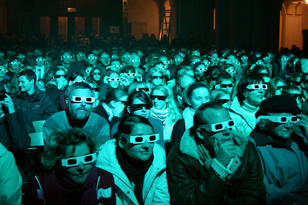 Nell'immagine: Persone in sala con occhiali 3D: tranquilli, per rivedere i nostri webinar non servono! Di Helmut Jilka, CC BY-SA 3.0, via Wikimedia Commons